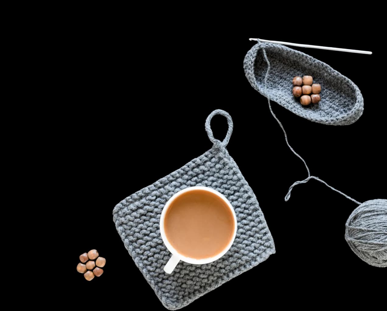 A crochet coaster with a cup of tea, a crochet basket, and a ball of yarn