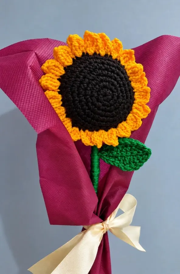 A crochet sunflower wrapped in magenta paper with a cream ribbon