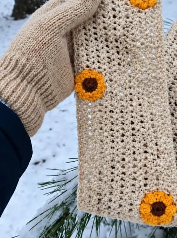 A cream crochet muffler with sunflower flowers, held in the snow