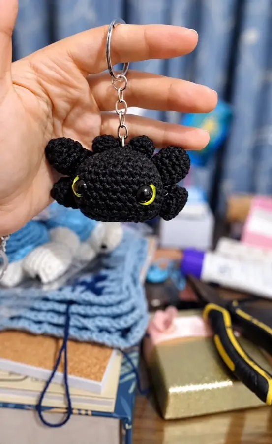 A black crochet dragon keychain held in a hand