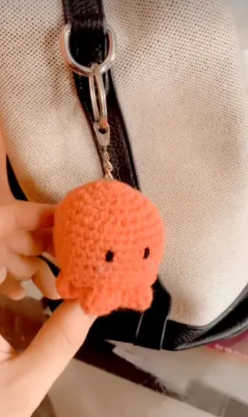 An orange crochet octopus keychain clipped to a bag