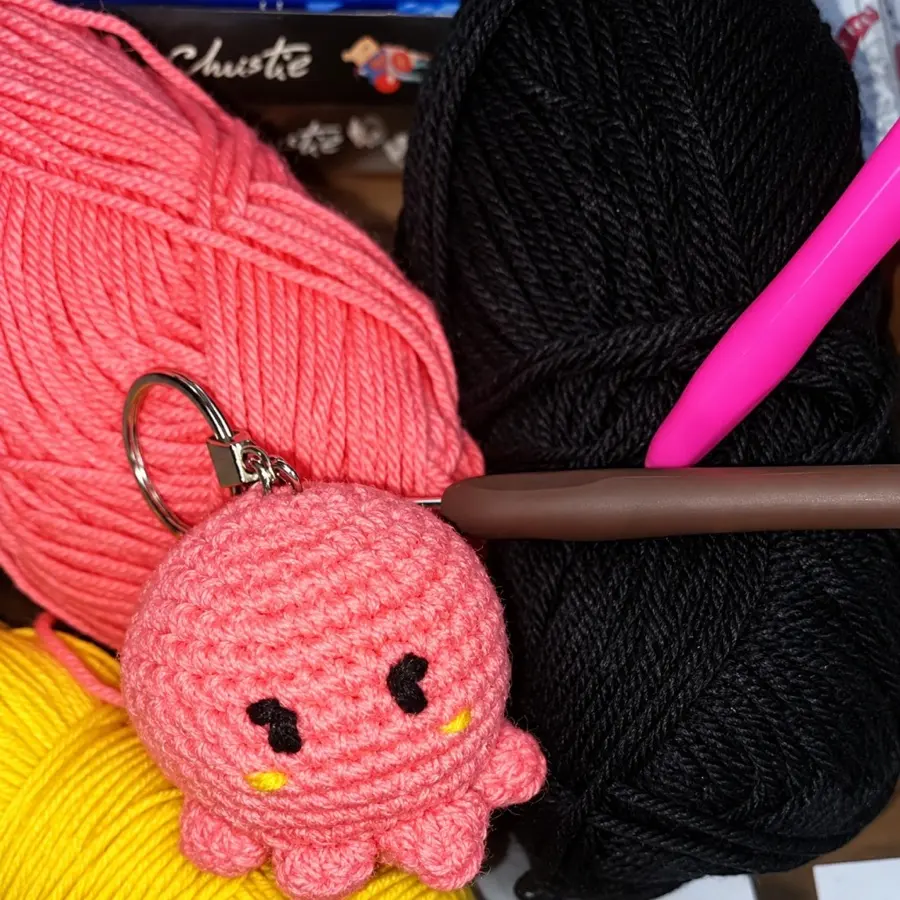 A pink crochet octopus keychain beside balls of yarn