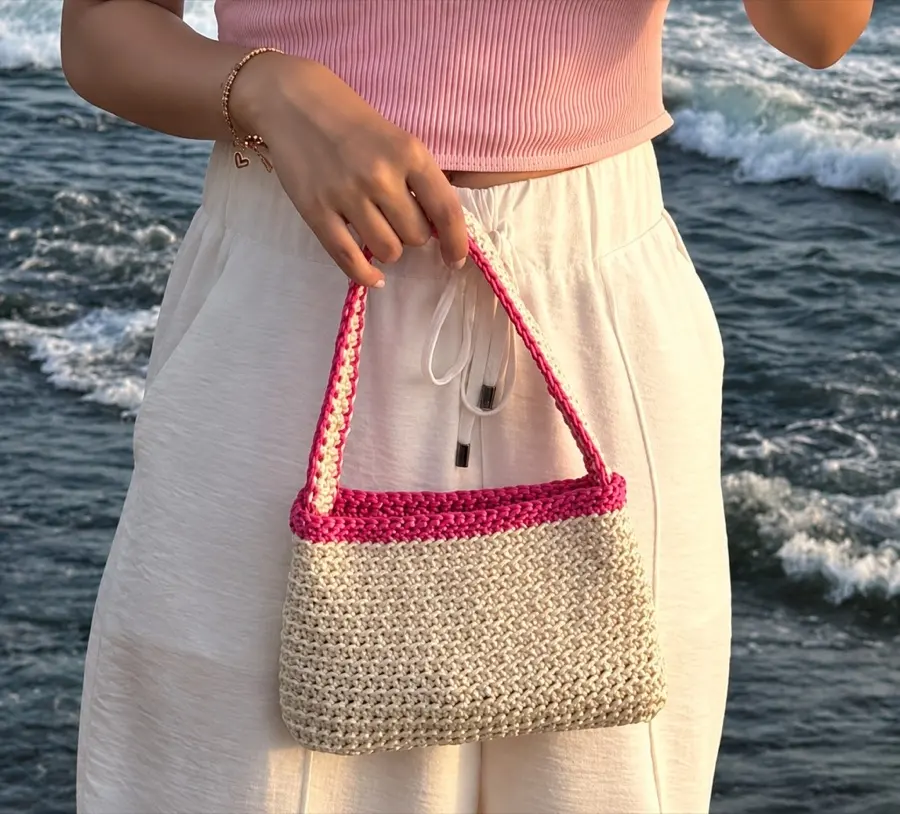 A cream crochet bag with pink trim held at the seaside